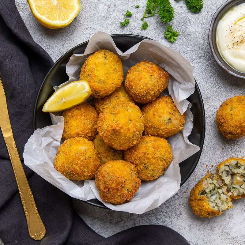 a bowl of cooked arancini with a lemon slice and a gold knife on grey background
