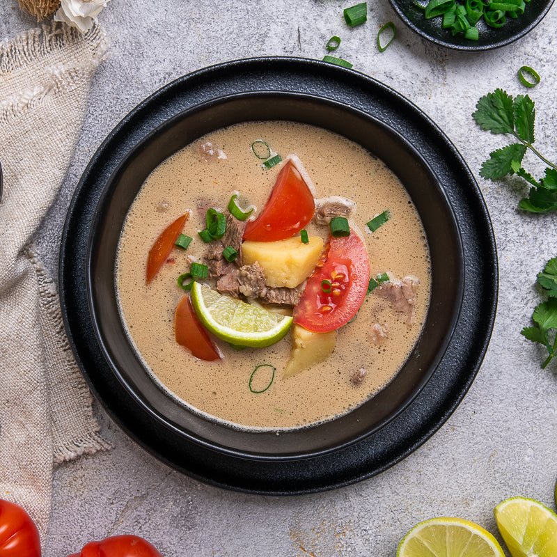 bowl of soup with tomatoes and lime on a gray surface