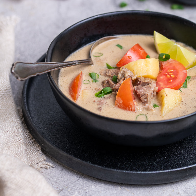 Black bowl of indonesian beef soup with vegetables and a spoon on a textured surface