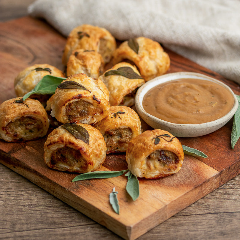 Baked turducken rolls with sage leaves on a wooden board with a side of mustard.