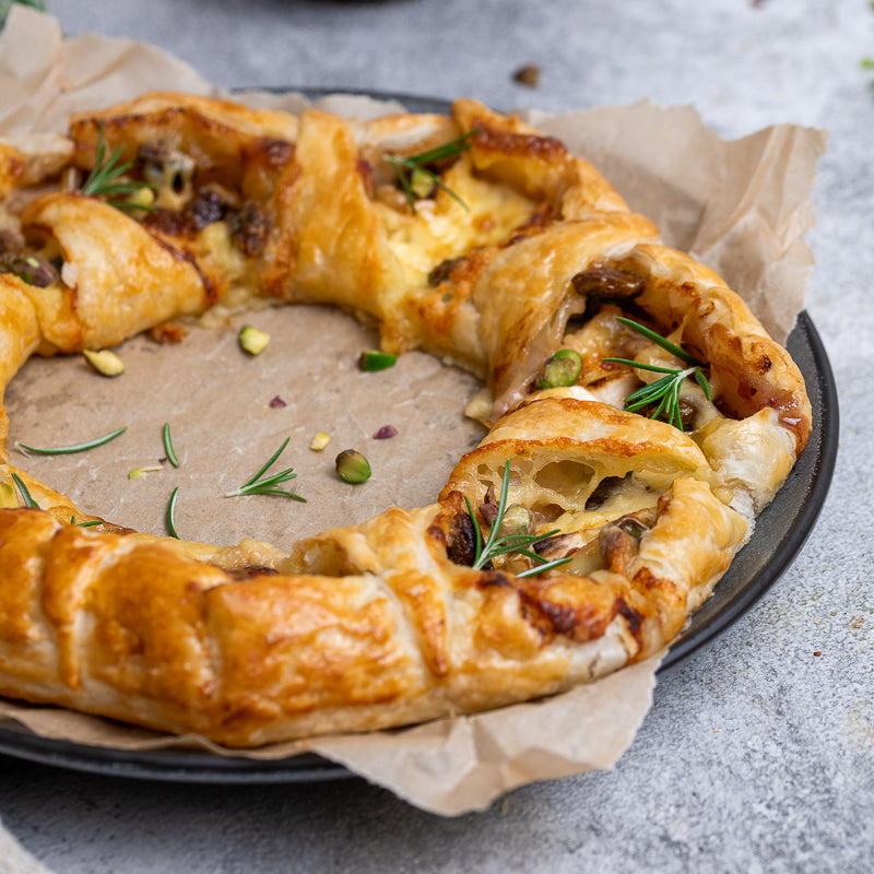 A side view of our Puff pastry christmas wreath with brie cheese, cranberry and herbs on a gray surface