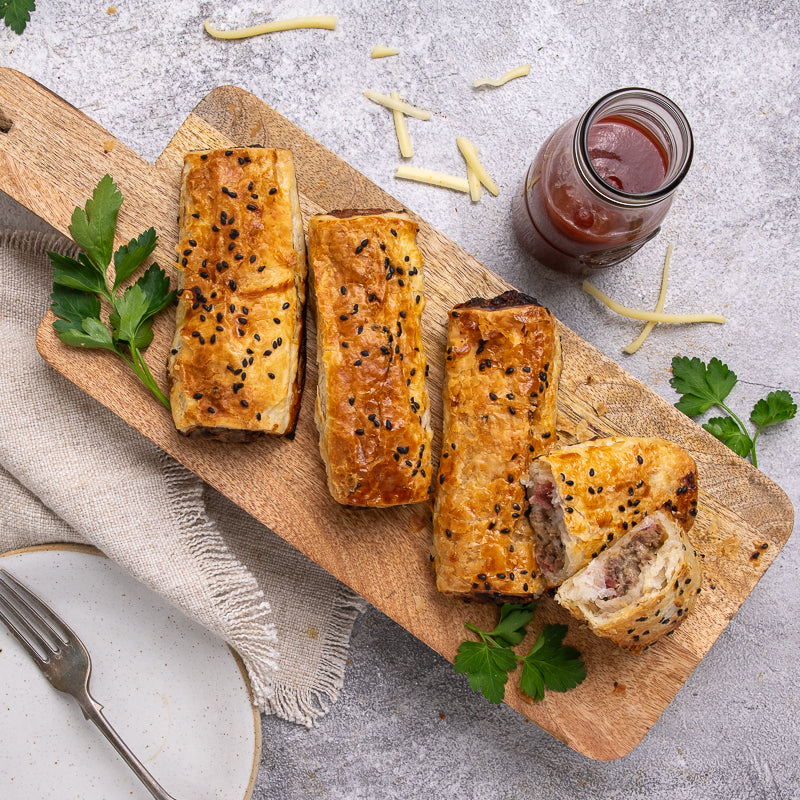 Beef Cheese and Bacon rolls on a wooden board with a jar of sauce and herbs on a gray surface.