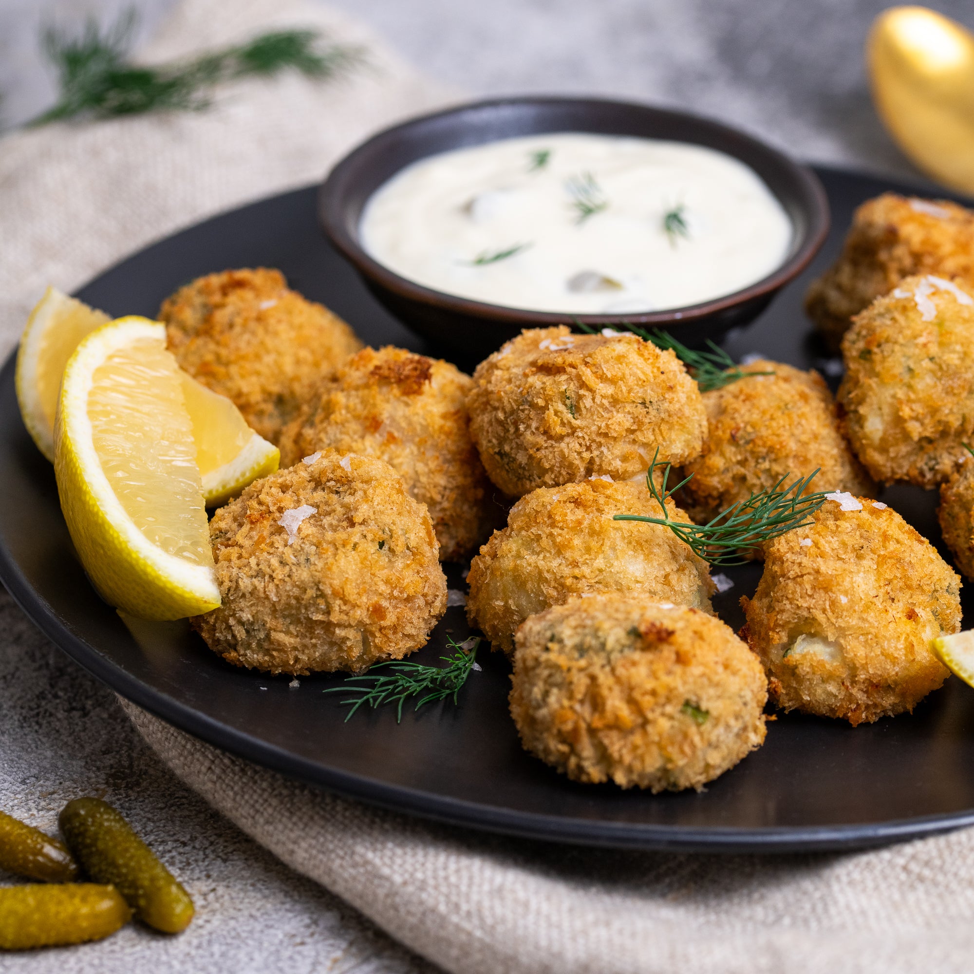 Barramundi fishcakes on a plate with lemon wedges and a side of dip.
