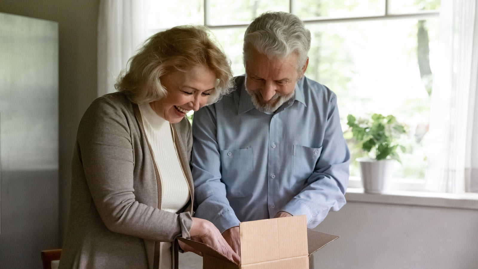 Senior couple opening a cardboard box together in a home setting.