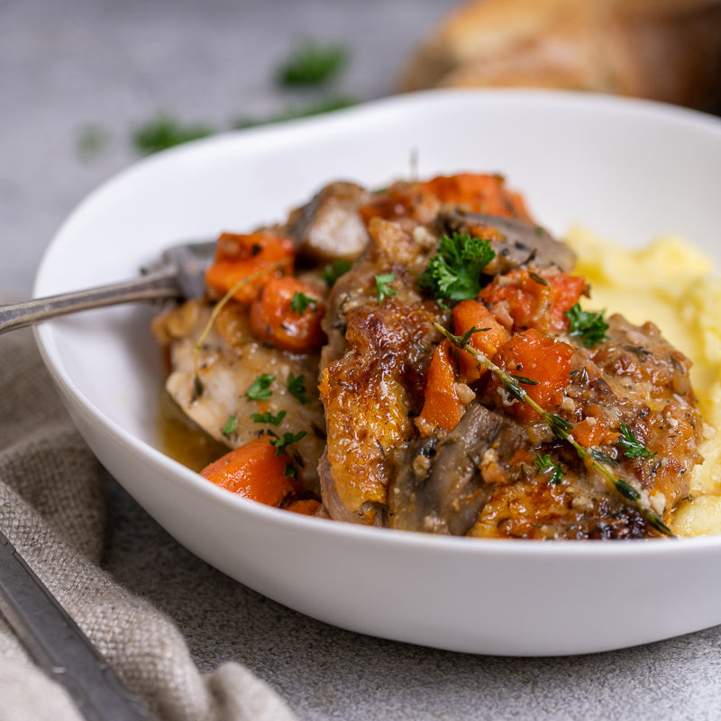 A plate of Chicken Cacciatore with mushrooms, carrots, and a rustic sauce served over mashed potatoes, garnished with parsley.