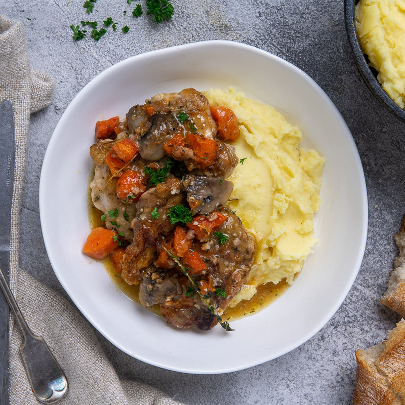 A plate of Chicken Cacciatore with mushrooms, carrots, and a rustic sauce served over mashed potatoes, garnished with parsley.