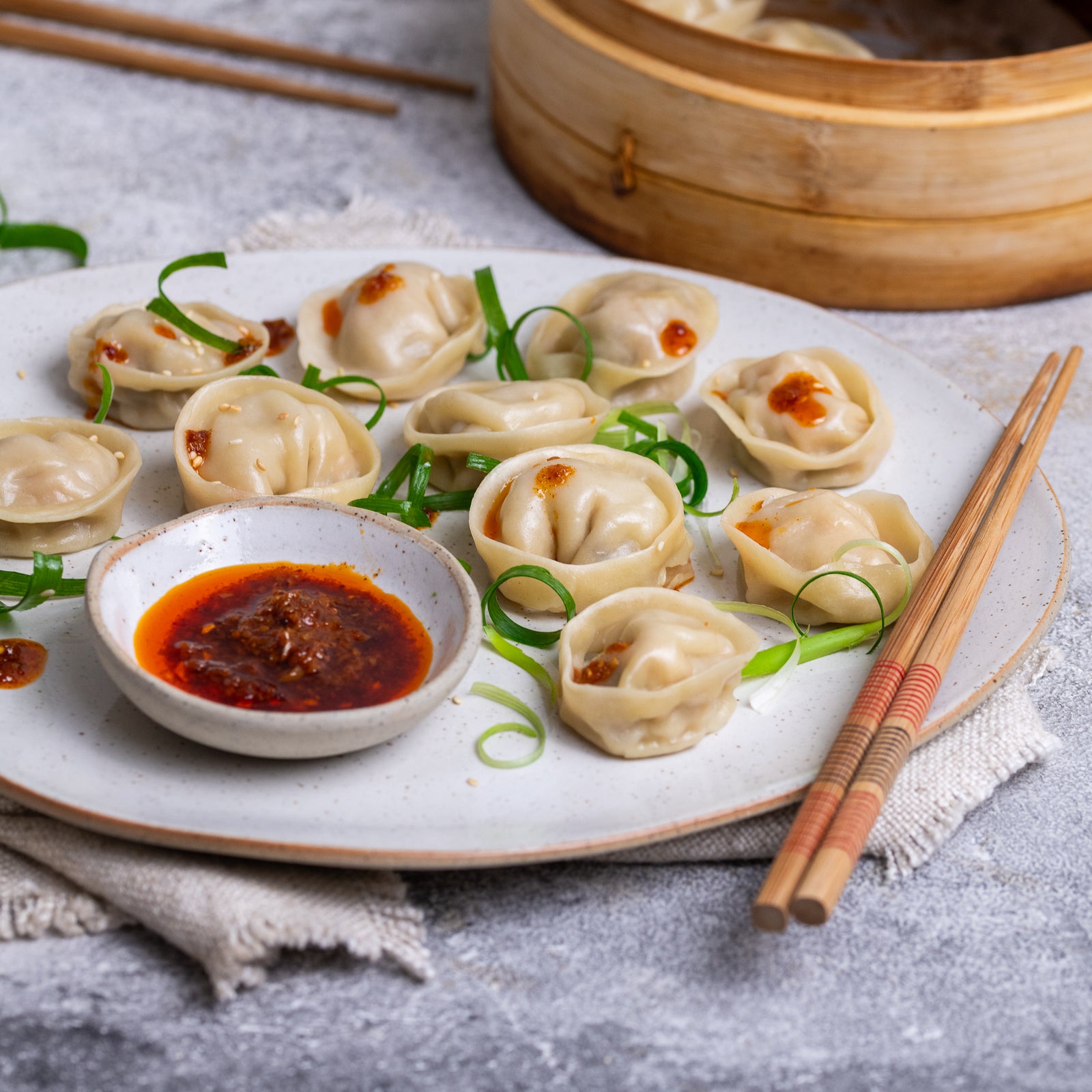 Platter of dumplings with dipping sauce and garnishes on a textured surface