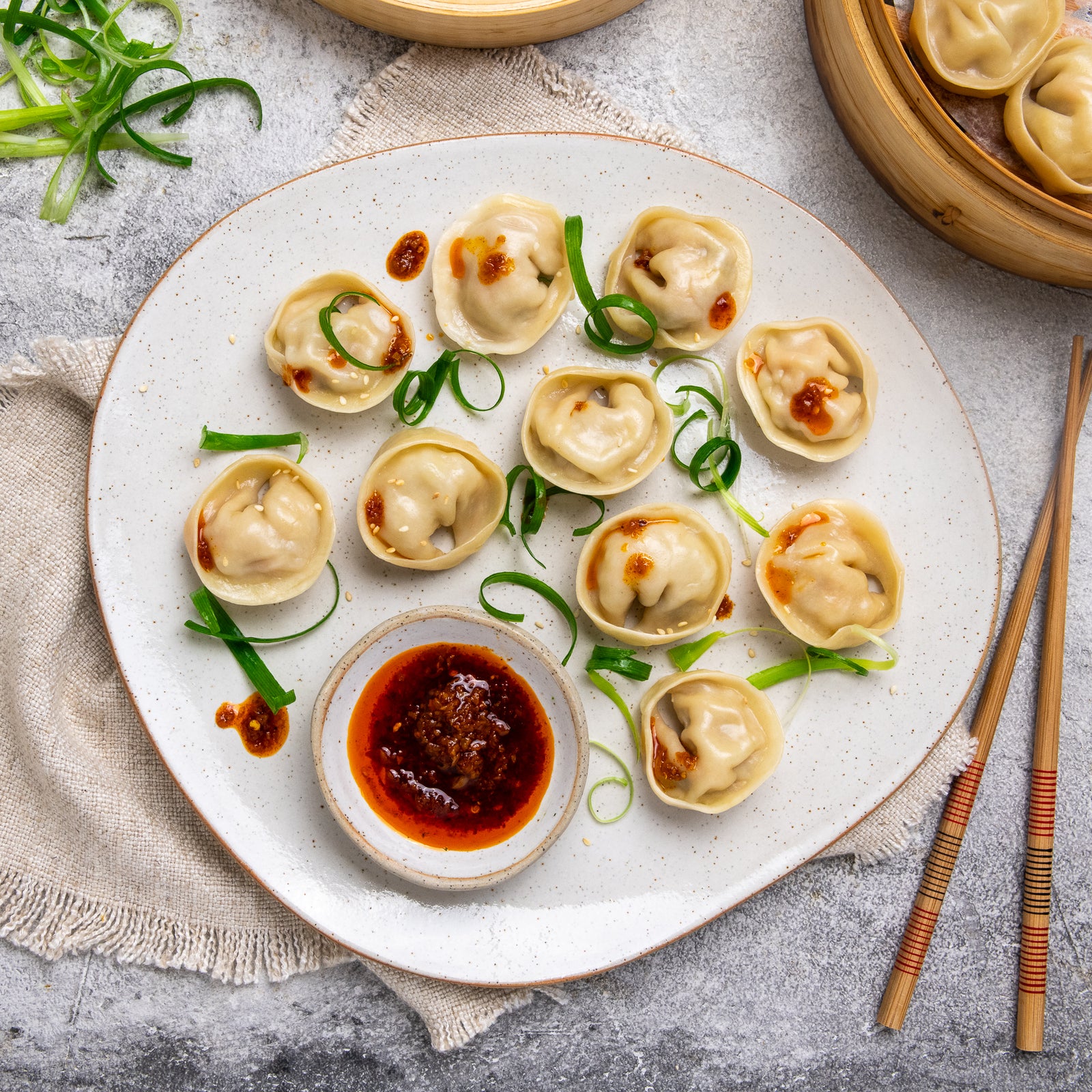 Platter of dumplings with dipping sauce and garnishes on a textured surface