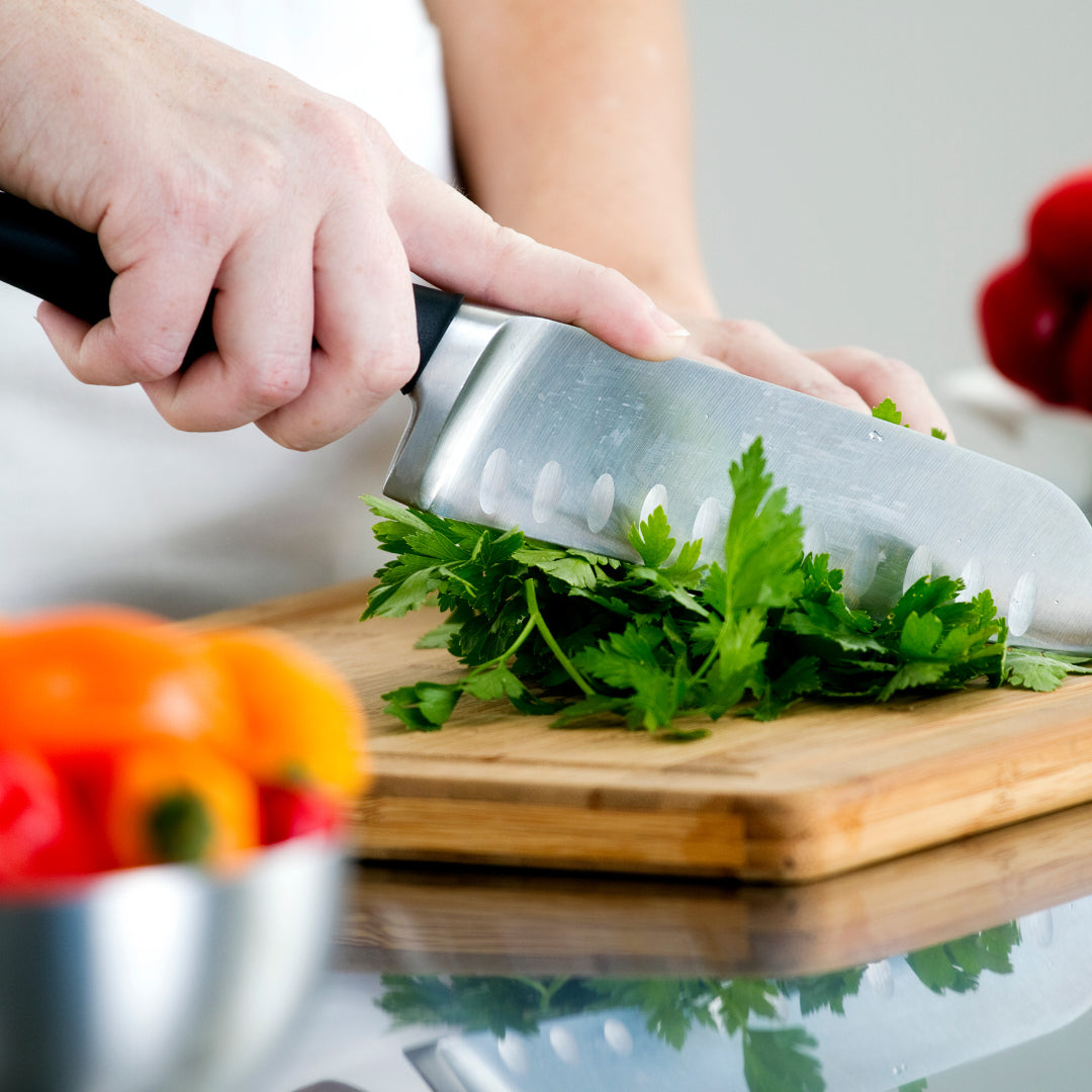Person cutting green herbs on a wooden cutting board with a knife.