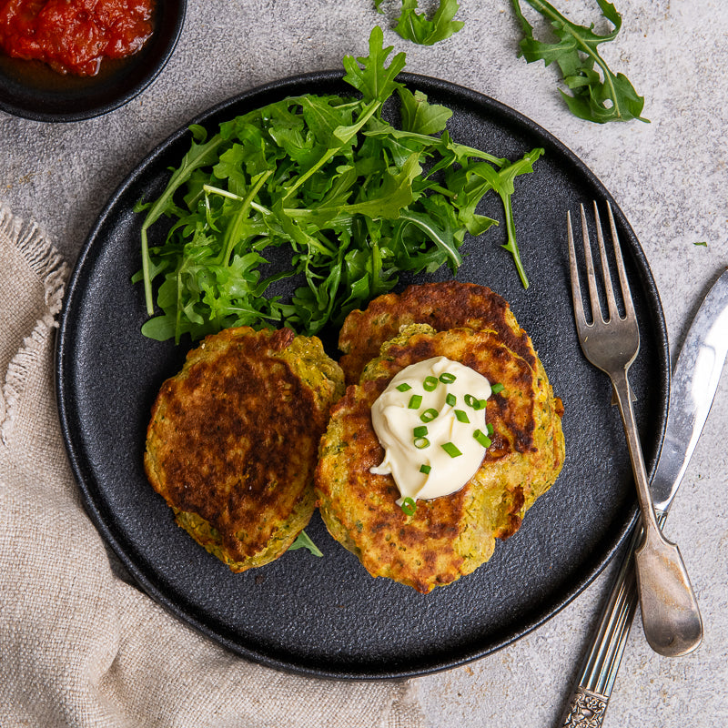 Stack of corn fritters on a black plate with arugula and sour cream garnish.