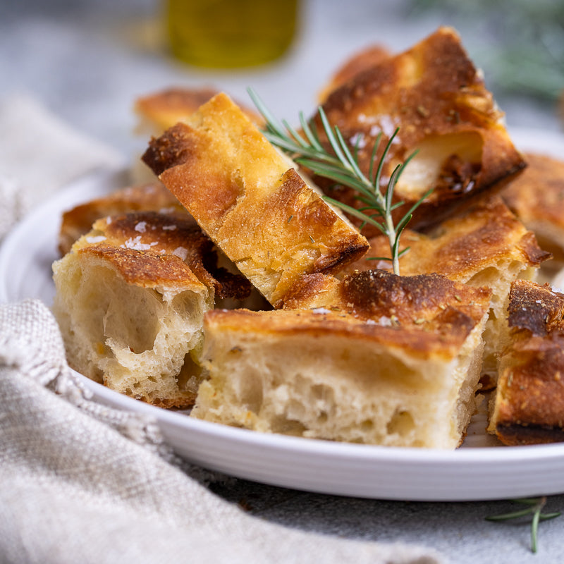 Platter of focaccia bread slices with a small bowl of olive oil and rosemary on a light background