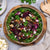 A prepared dish of French lentils, roast beetroots, caramelised red onion, walnuts, and marinaded feta, served on a bed of greens in a wooden bowl.