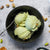 A bowl of Yogurt Sour Cherry Gelato with a spoon and cherries on a gray background