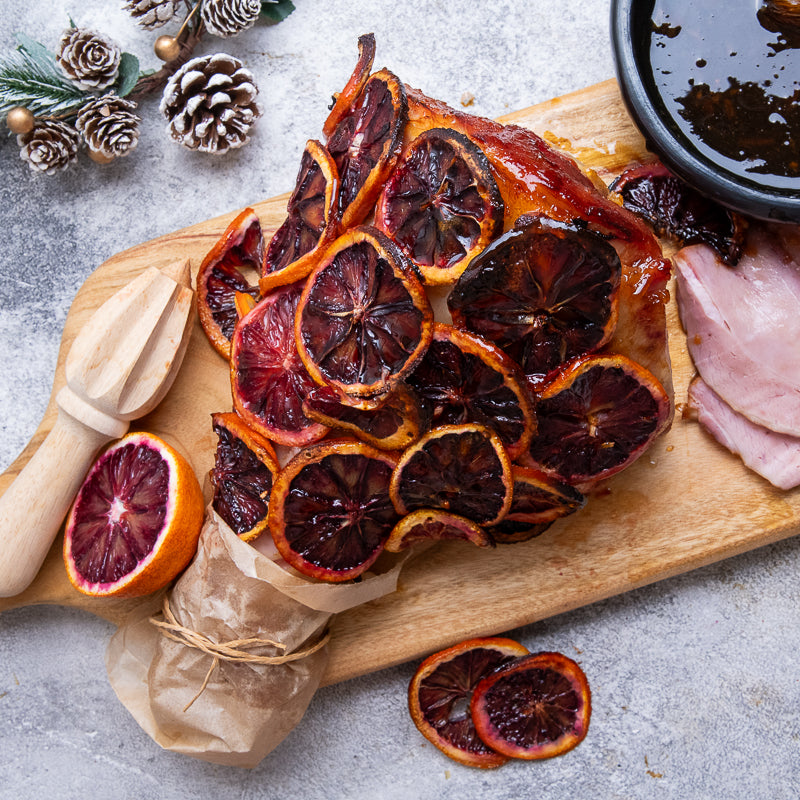 Dried blood oranges on a wooden board with a small bowl of glaze and a citrus reamer.