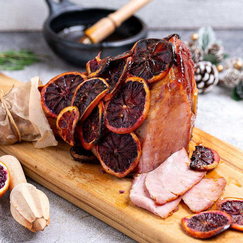 Dried blood oranges on a wooden board with a small bowl of glaze and a citrus reamer.