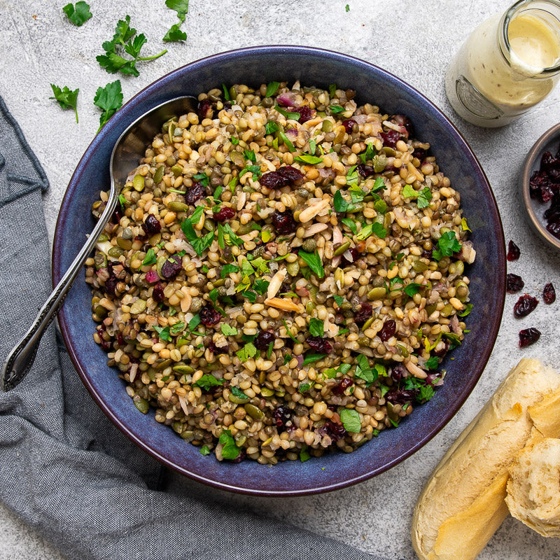 A prepared cypriot grain salad dish served in a bowl, garnished with herbs and accompanied by a side of yogurt dressing and bread.