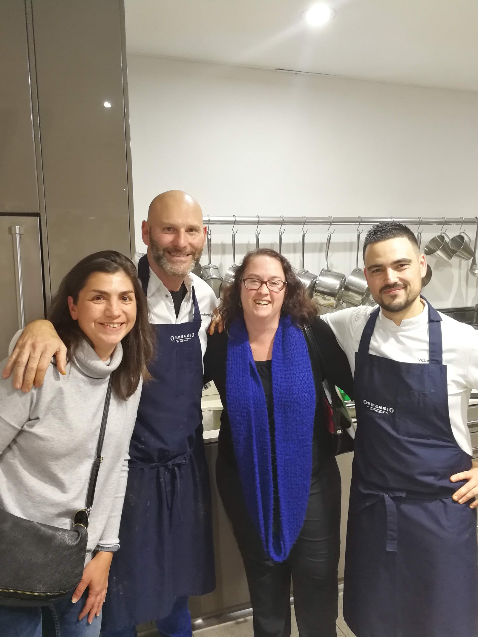 Four people posing together in a kitchen, two wearing aprons.