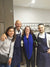 Four people posing together in a kitchen, two wearing aprons.