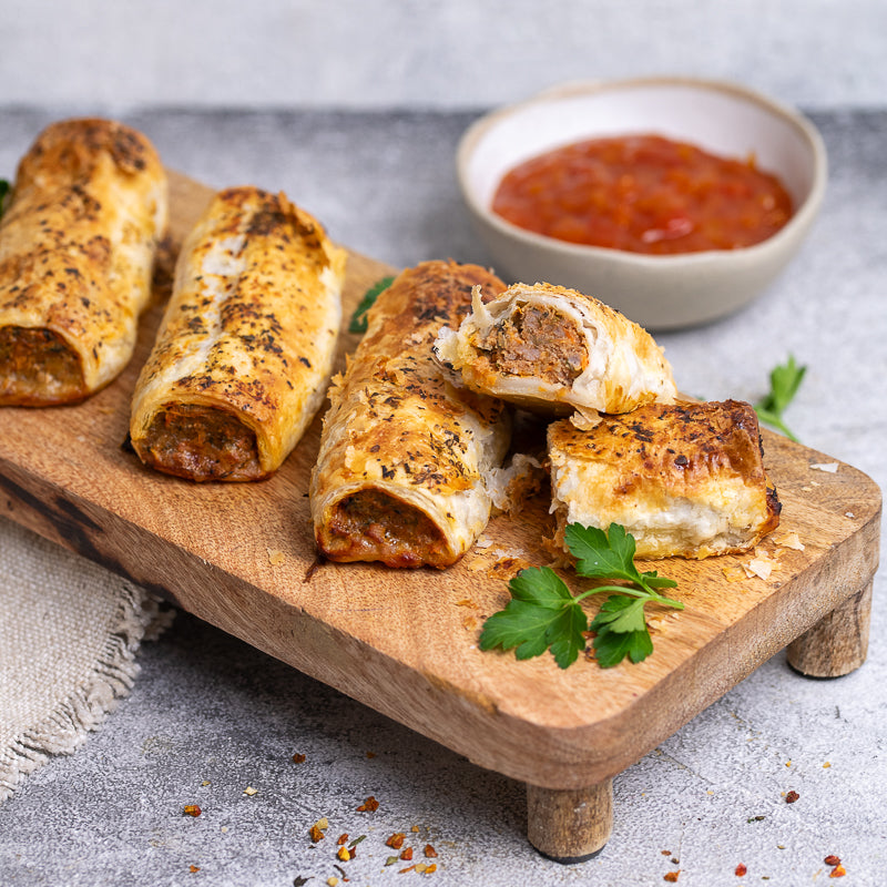 Italian Meatball sausage rolls on a wooden board with a side of red sauce.
