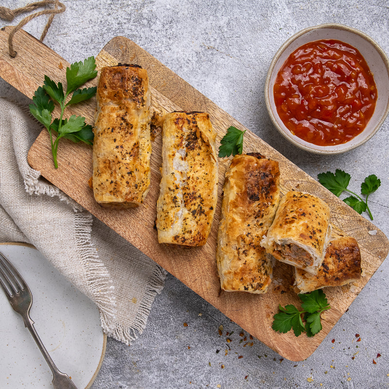 Italian Meatball sausage rolls on a wooden board with a side of red sauce.