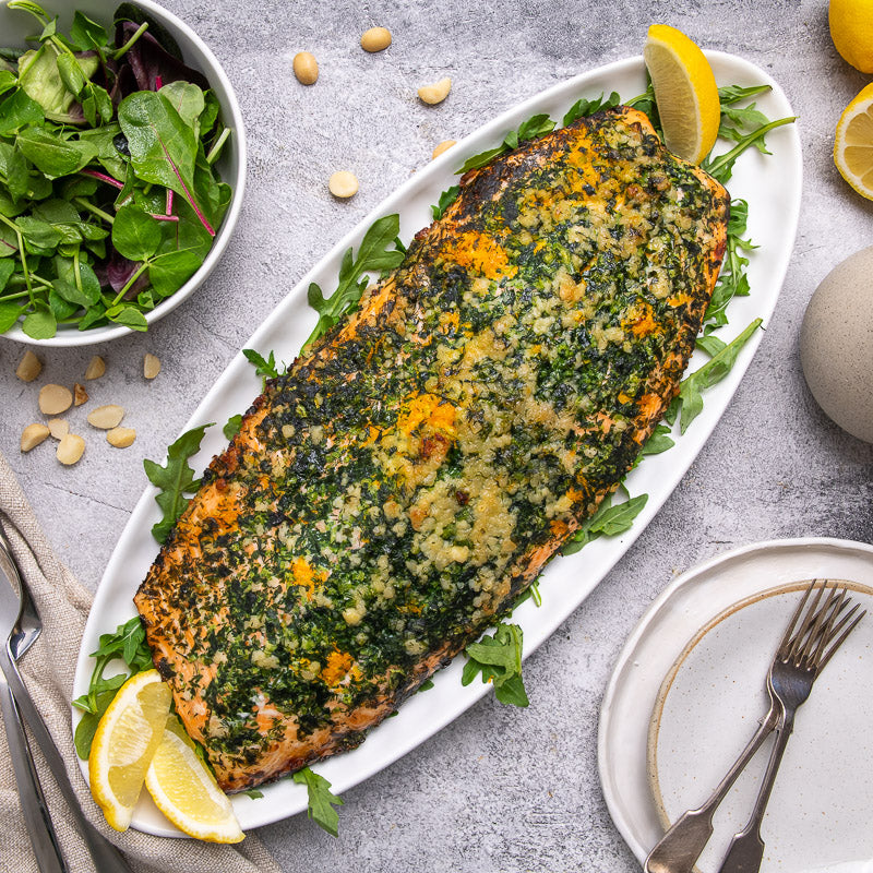 A salmon fillet with macadamia crust on a bed of greens, being drizzled with lemon myrtle velouté sauce.