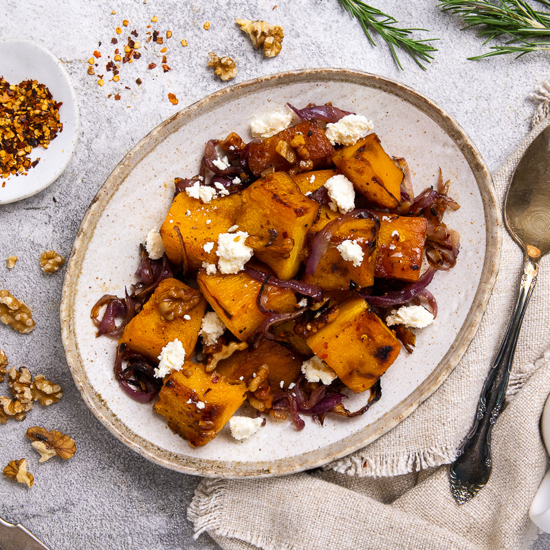 Plate of roasted pumpkin cubes with maple syrup onions and feta cheese on a textured surface.