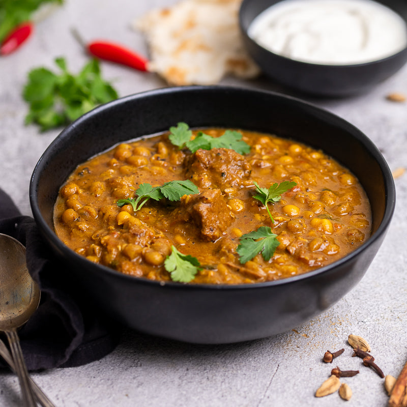 Bowl of mutton and lentil curry with rice and spices on a gray surface