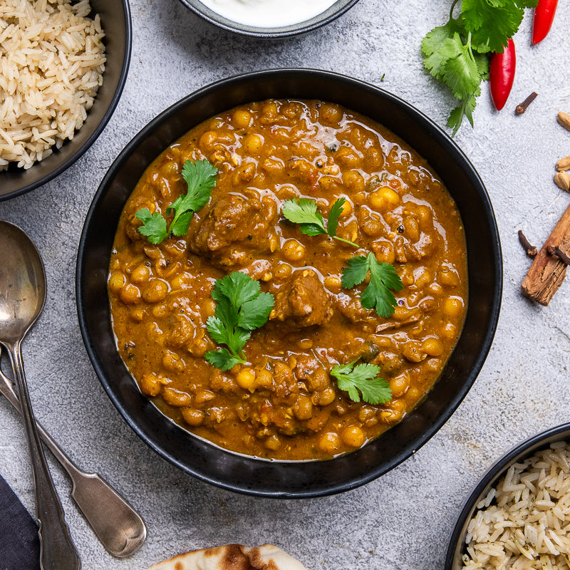 Bowl of mutton and lentil curry with rice and spices on a gray surface