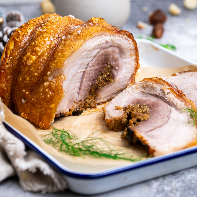 Sliced roasted pork belly on a white plate with a blue rim, garnished with green herbs.