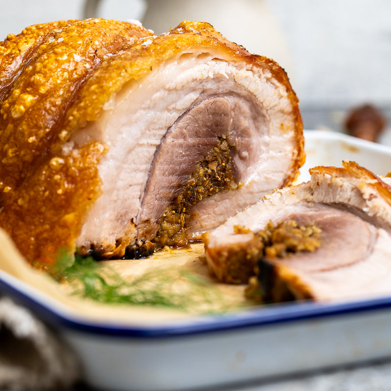 Close-up of roasted pork belly with a crispy skin on a white plate.