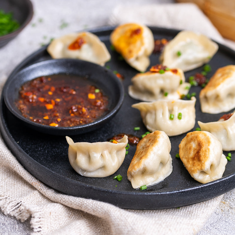 Dumplings on a black plate with a small bowl of dipping sauce.