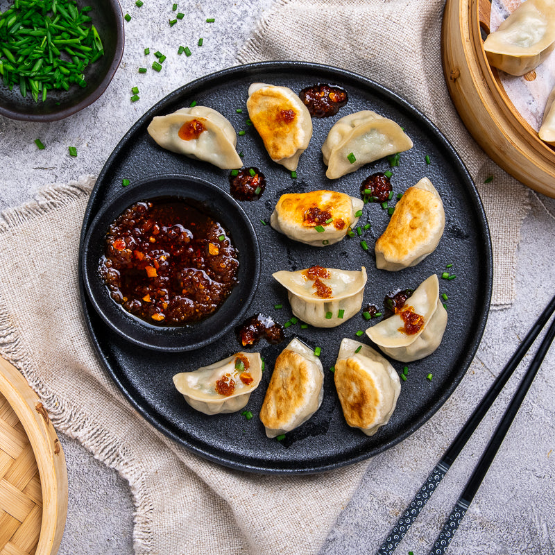 Plated dumplings with a side of dipping sauce on a textured surface