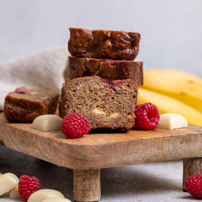 Loaf of banana bread with slices on a wooden board with raspberries and bananas.