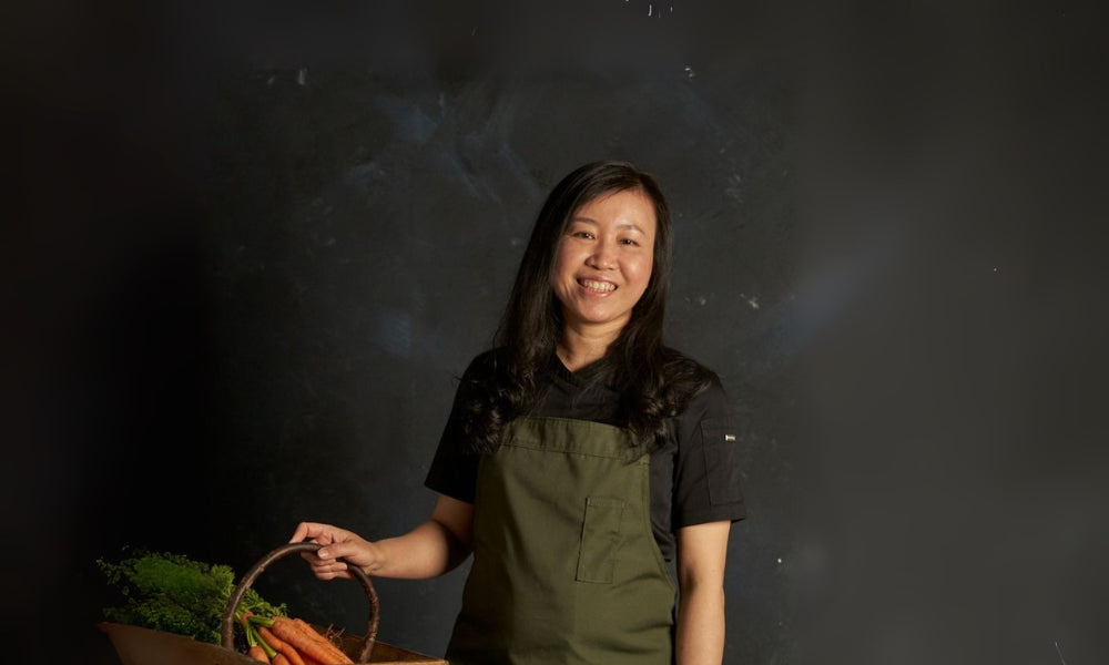 FoodSt cook Iris holding a basket of carrots against a dark background