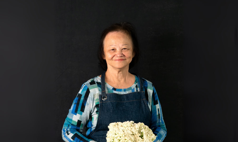 Image of FoodSt cook Christina holding a cauliflower against a black background