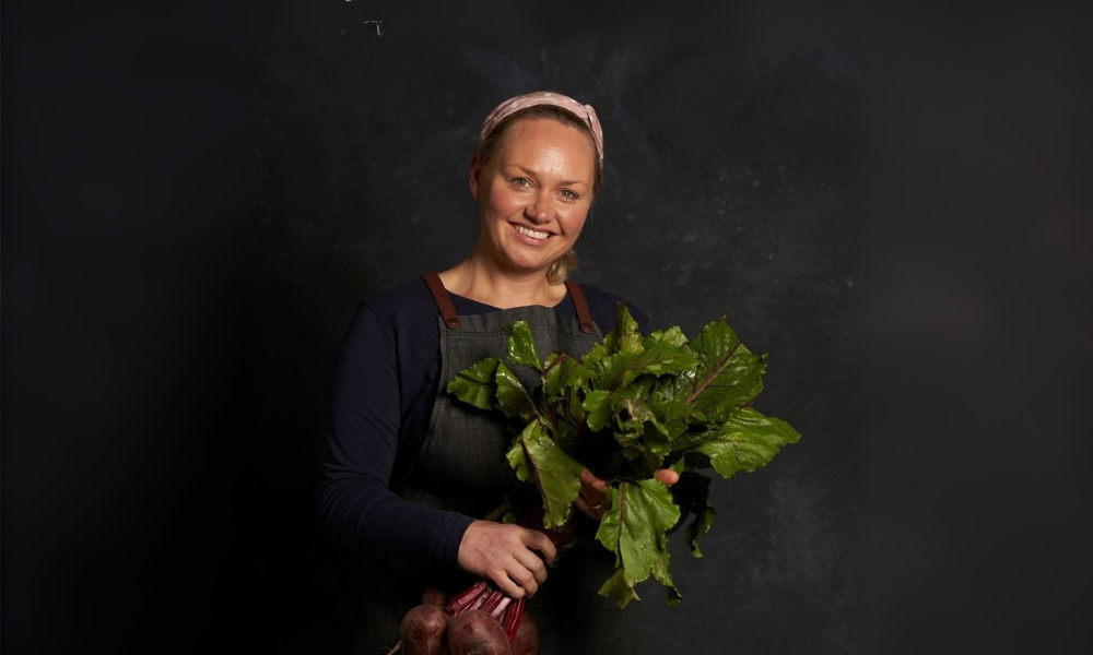 FoodSt cook Helen holding a bunch of green leafy vegetables against a dark background