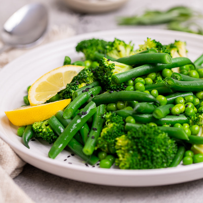 Plate of green vegetables with lemon slices on a light background