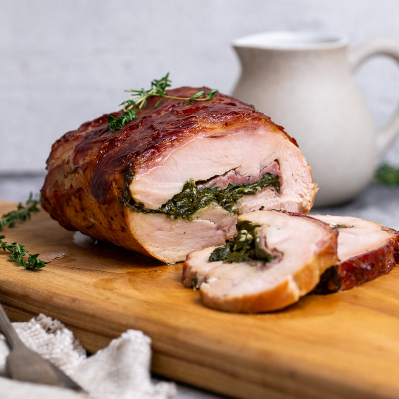 Turkey wrapped in prosciutto Christmas roast with spinach filling on a wooden board, with a blurred background.