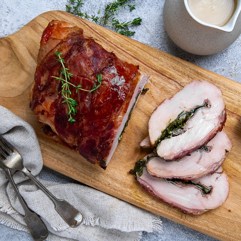 Turkey wrapped in prosciutto Christmas roast with spinach filling on a wooden board, with a blurred background.
