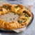 Pastry wreath with cranberry and brie and herbs on a gray surface