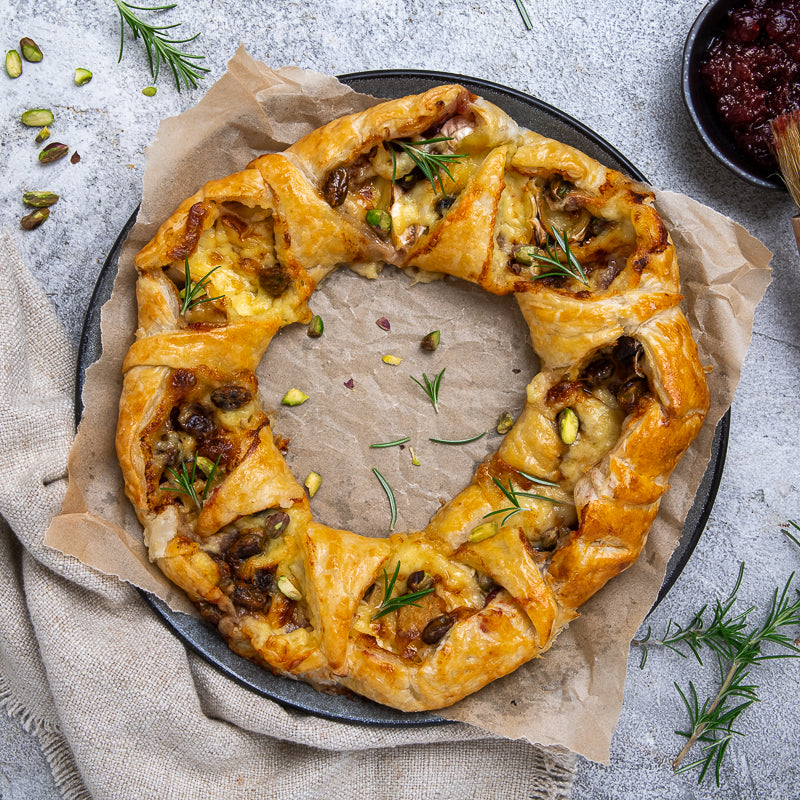 Pastry wreath with cranberry and brie and herbs on a gray surface