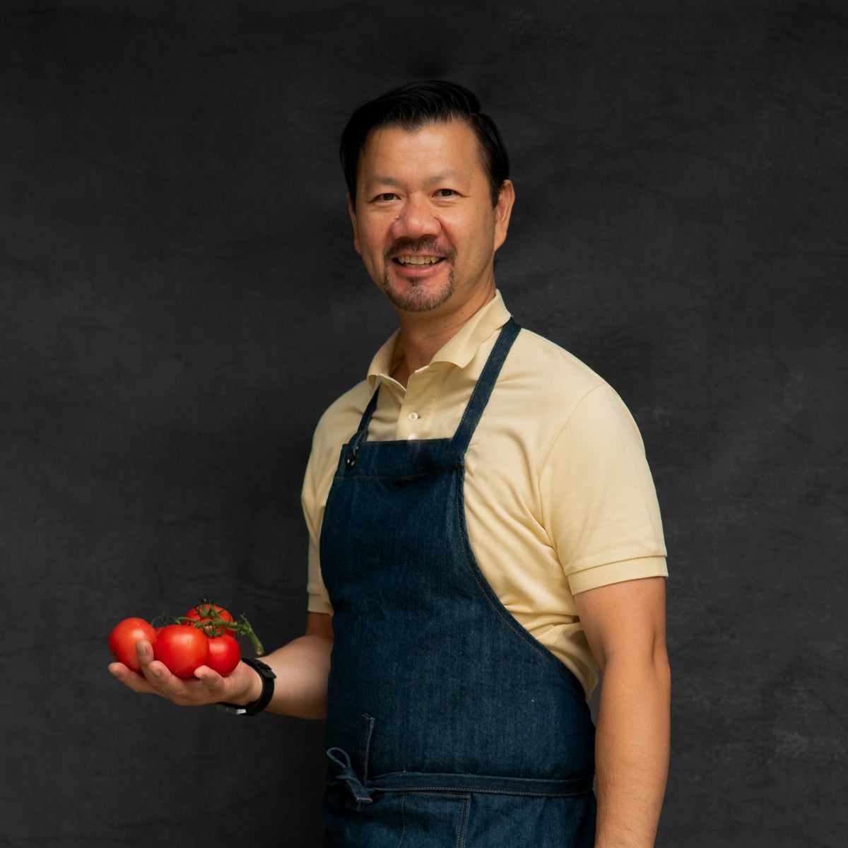 A portrait of Ben, FoodSt Cook holding tomatoes  against a black background